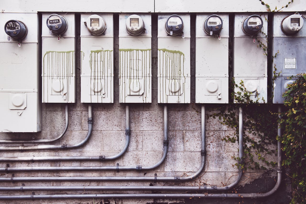 Array of outdoor electric meters on a brick wall with vines.